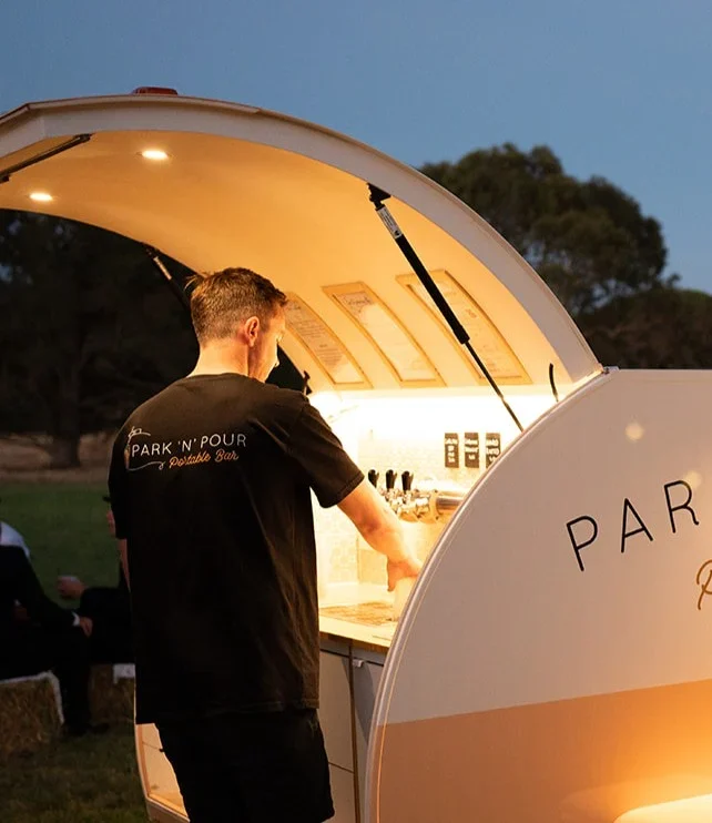Park 'n' Pour bar staff member in a branded shirt pouring drinks from the Teardrop Bar taps at dusk