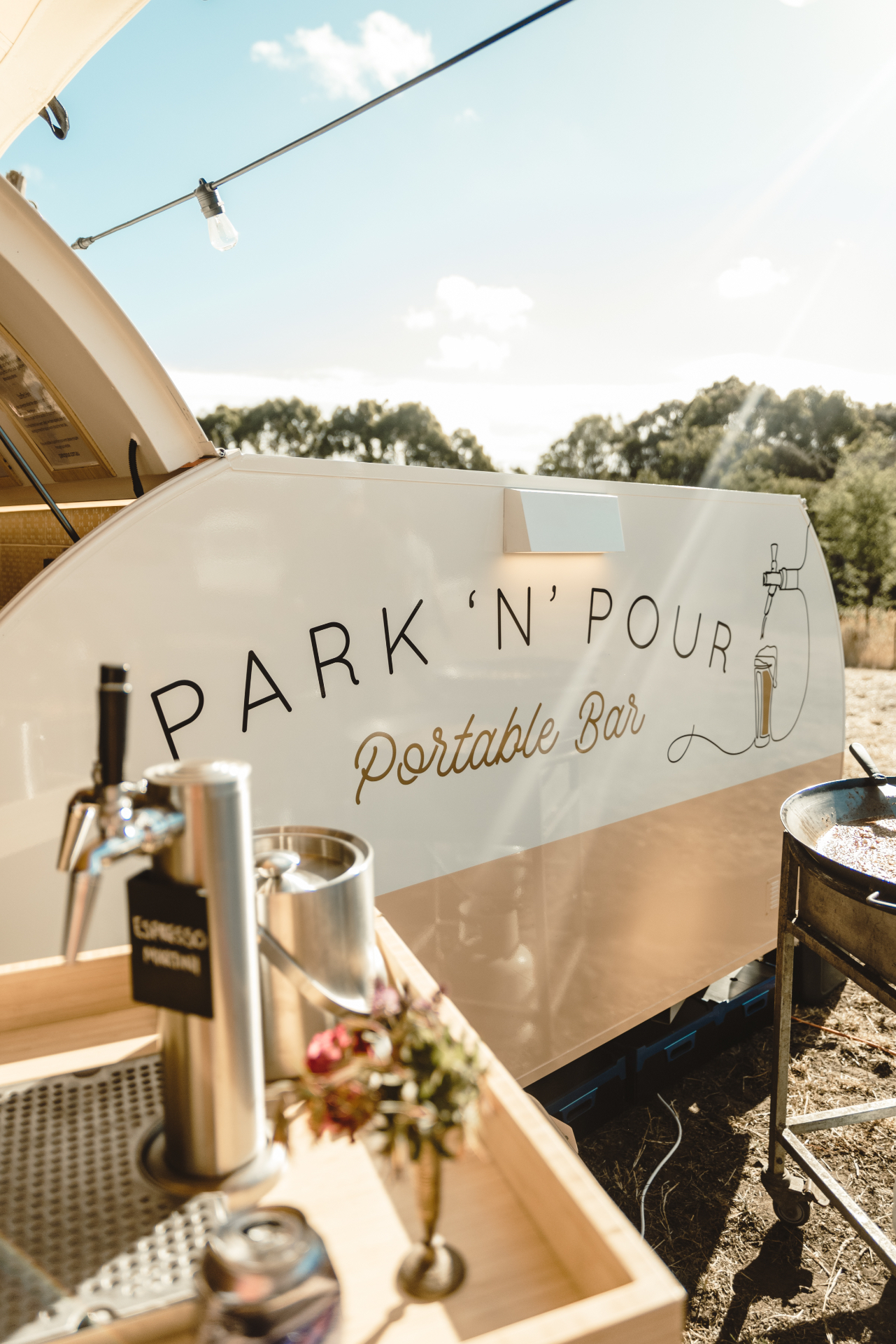 Sunny side shot of the Park 'n' Pour teardrop bar, logo on the side panel, beer tap in the foreground under a festoon light